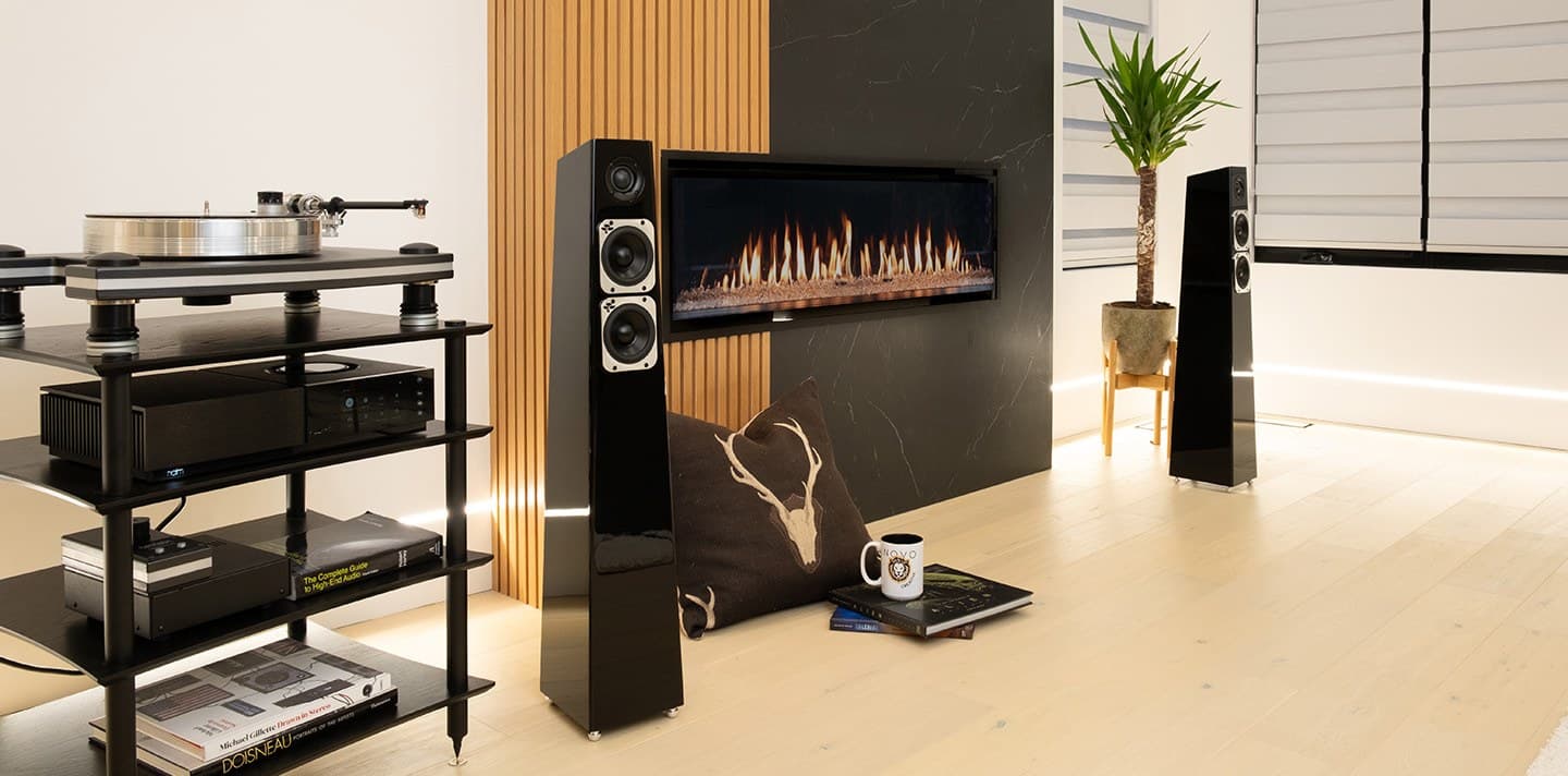 Totem Acoustic Tribe Tower loudspeakers in gloss black beside a turntable and a linear fireplace
