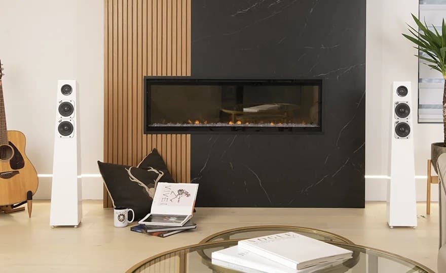 Totem Acoustic Tribe Tower loudspeakers in white flanking a fireplace wall of wood slats and dark stone